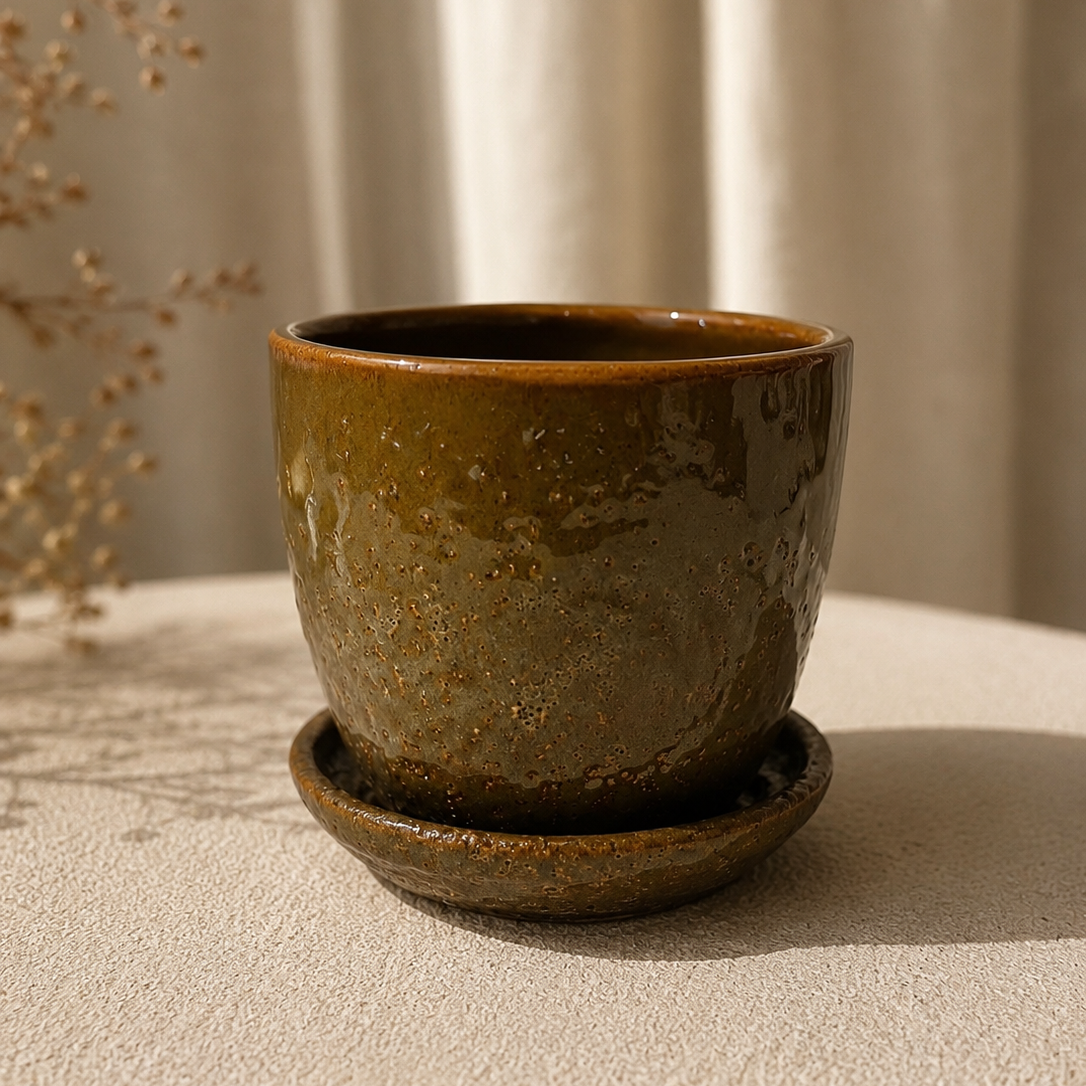 A small handmade ceramic pot with a matching saucer, featuring a textured earthy brown and olive-green glaze.
