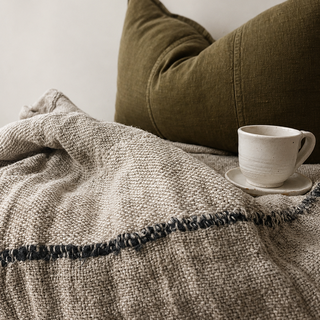 Cozy scene with a textured blanket, green pillow, and white mug on a saucer.