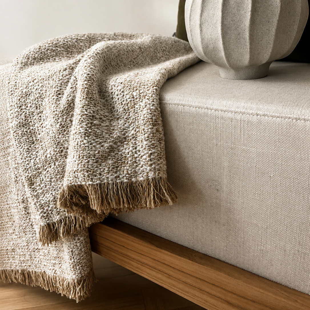 Beige textured blanket draped over a light gray sofa with a decorative vase.